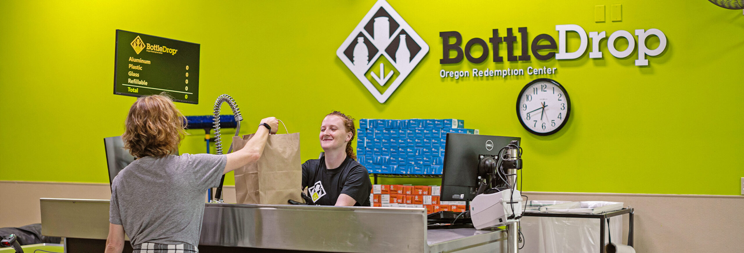 A BottleDrop employee receiving a bag of recyclables from a customer.