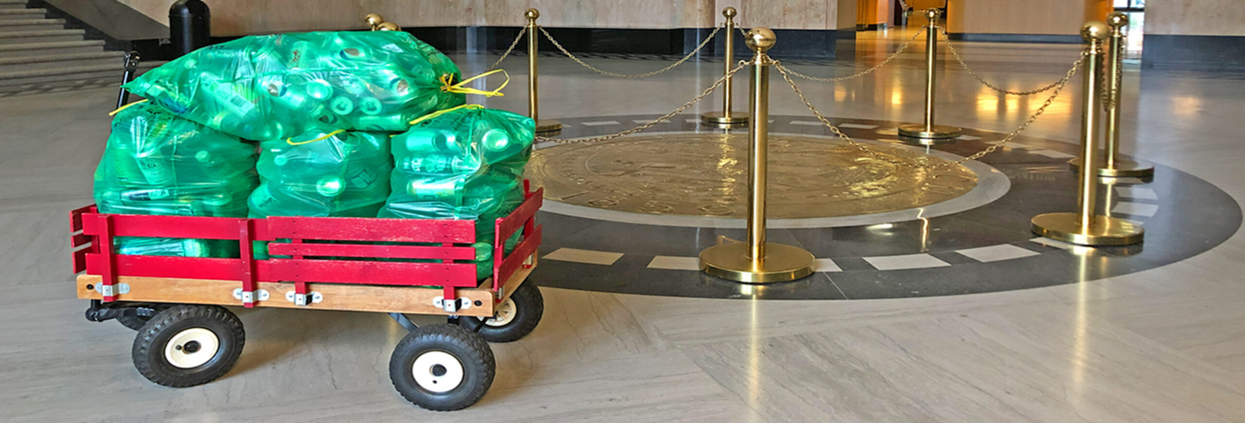 Green bags of recyclable containers in a small red wagon inside the Oregon State Capitol.