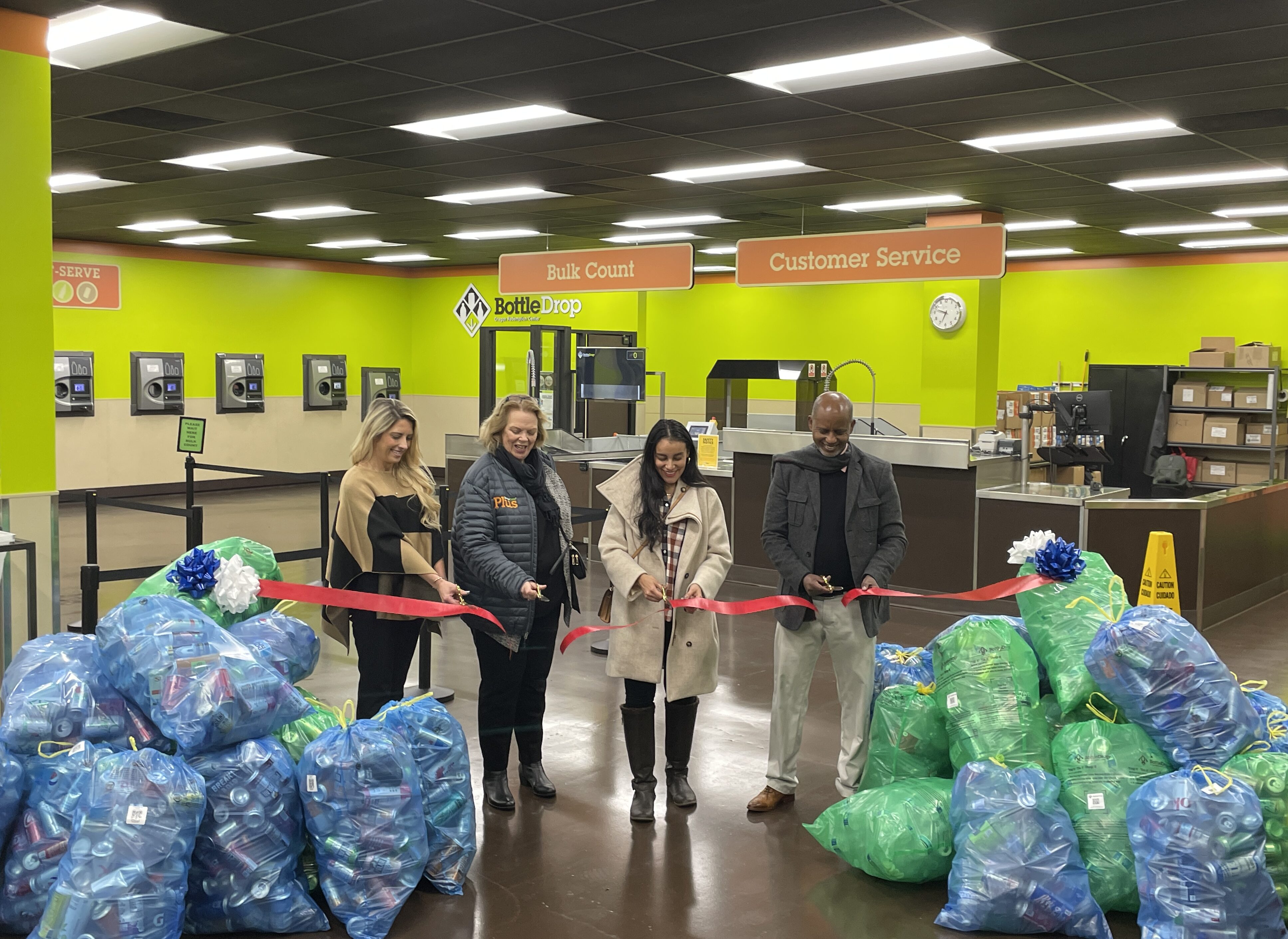 Photo is the ribbon cutting done by four people inside a brand new BottleDrop redemption center.