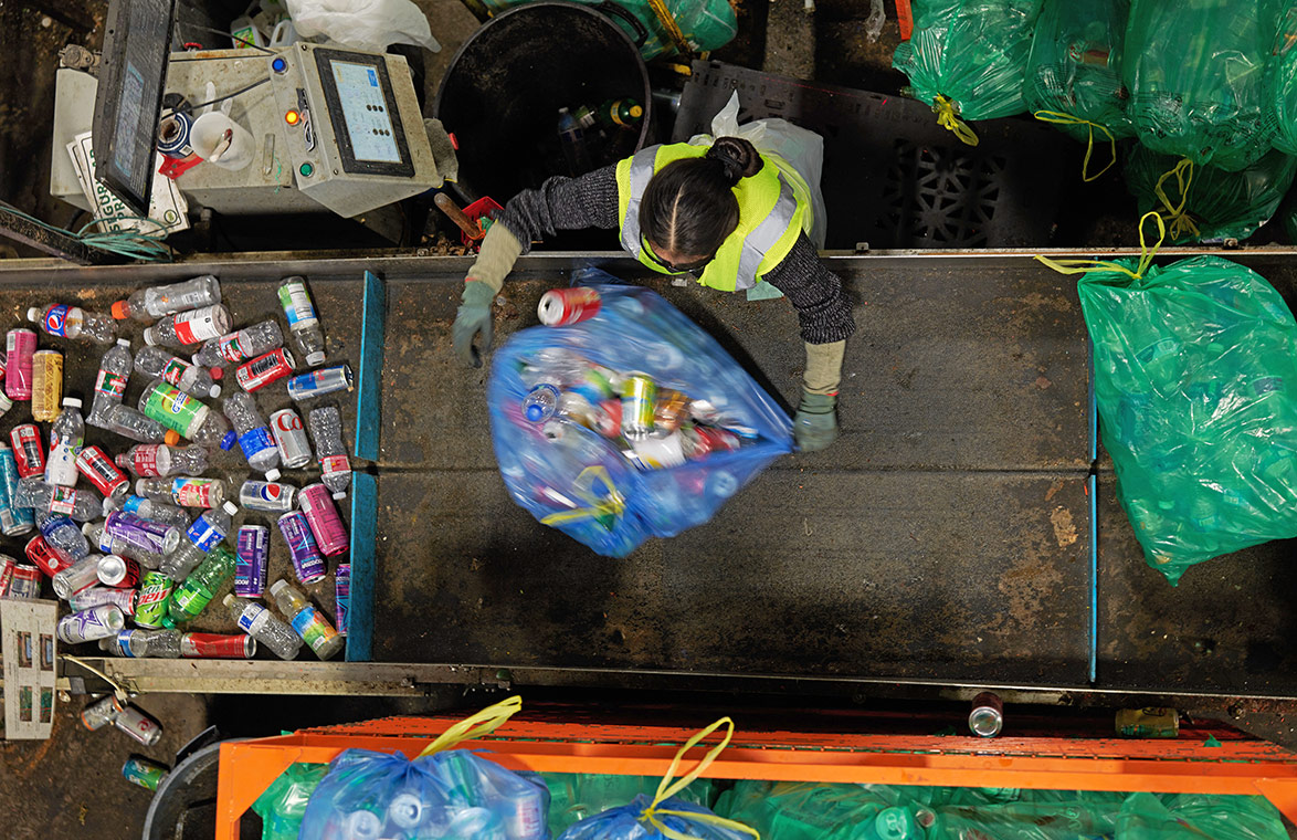 Seen from above, an OBRC employee opens a blue bag of recyclable containers onto a sorting tray.
